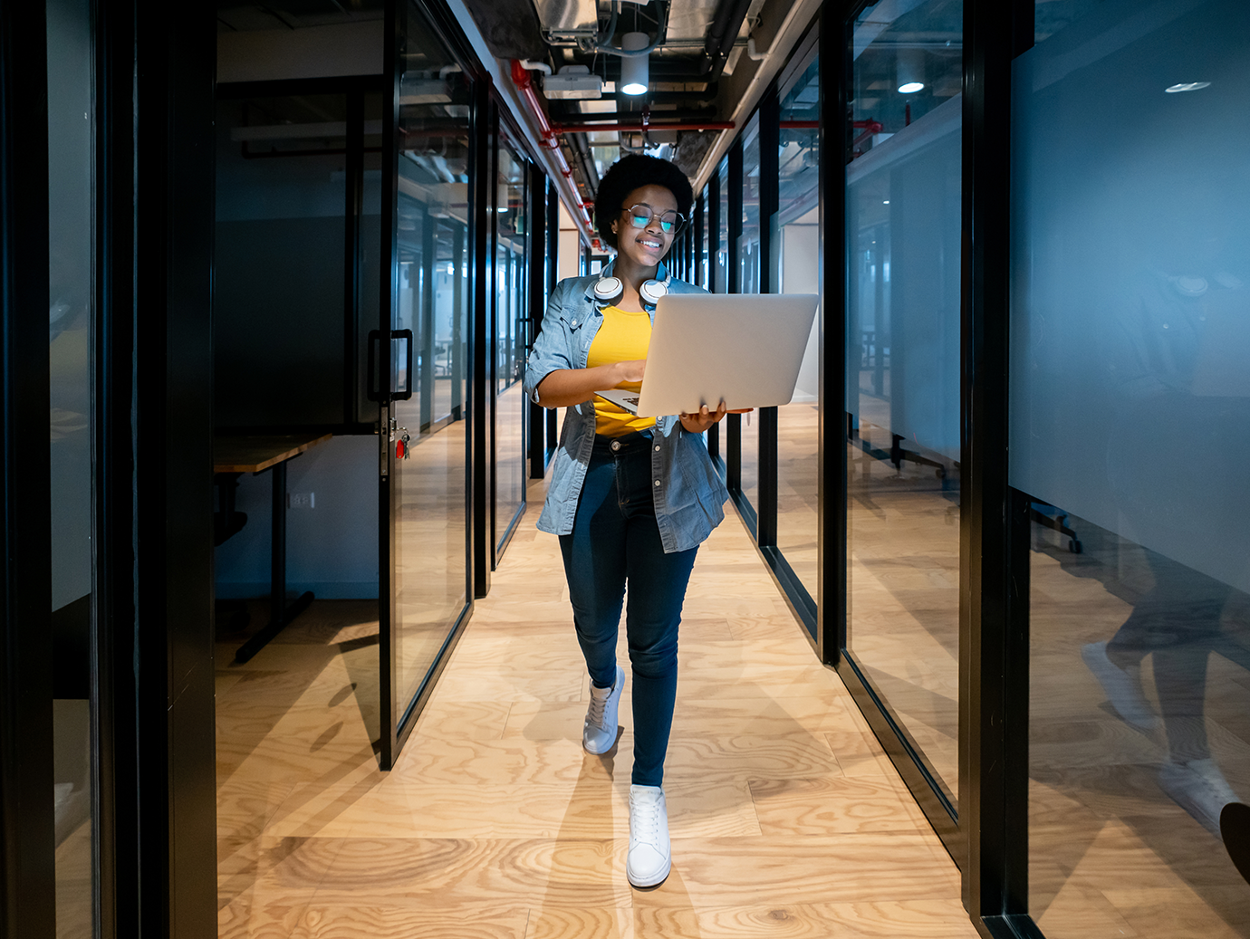 A woman walking in a lobby between conference rooms holding a laptop